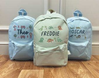 May include: Three light blue and mint green backpacks with personalized names and themed illustrations. The light blue backpacks feature the names "Theo" and "Oscar" with fire truck and animal graphics. The mint green backpack has the name "Freddie" with dinosaur graphics.
