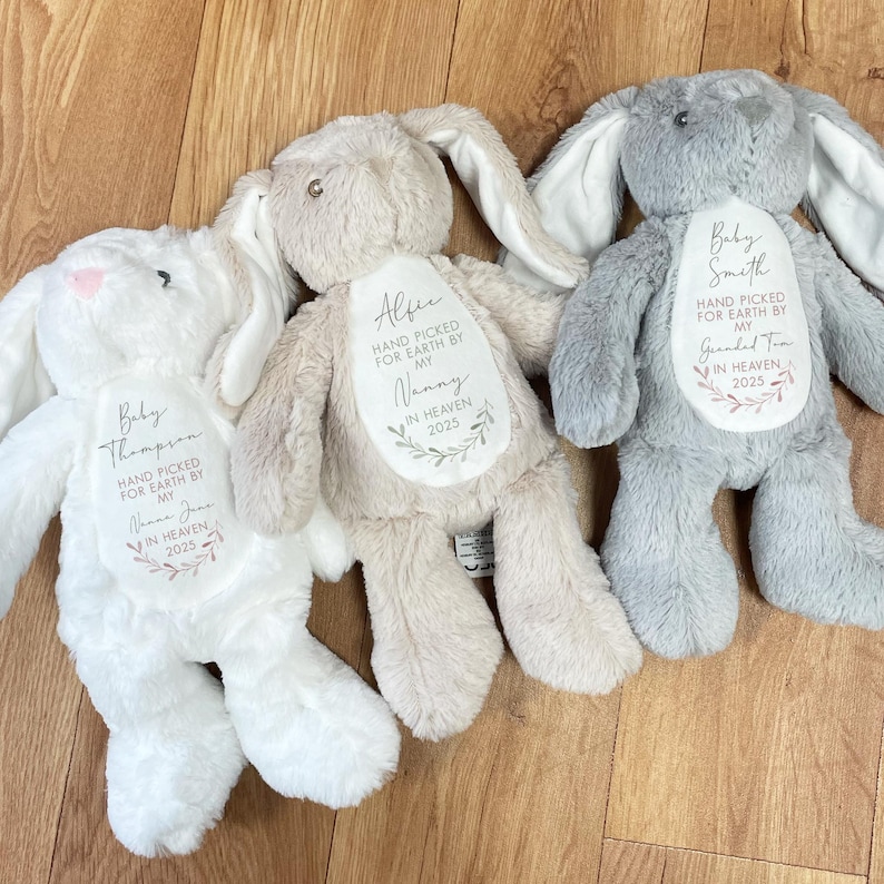 May include: Three plush bunny toys with embroidered messages. The white bunny says "Baby Thompson, Hand Picked for Earth by My Nana June, In Heaven 2025". The beige bunny says "Alfie, Hand Picked for Earth by My Nanny, In Heaven 2025". The gray bunny says "Baby Smith, Hand Picked for Earth by My Grandma Tim, In Heaven 2025".