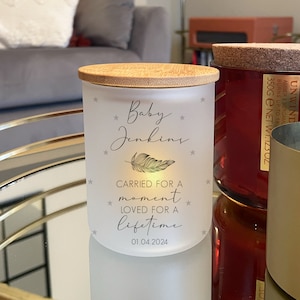 May include: White frosted glass candle jar with a bamboo lid. The jar has a black and gold feather design and the text "Baby Jenkins * CARRIED FOR A moment * LOVED FOR A lifetime * 01.04.2024"