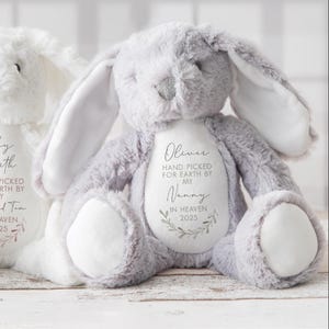 May include: A gray plush bunny with white accents. The bunny has a white patch on its chest with the text "Oliver Hand Picked for Earth by My Nanny In Heaven 2025".