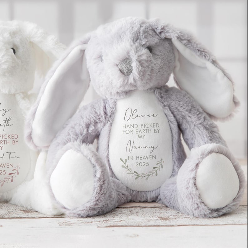 May include: A gray plush bunny with white accents. The bunny has a white patch on its chest with the text "Oliver Hand Picked for Earth by My Nanny In Heaven 2025".