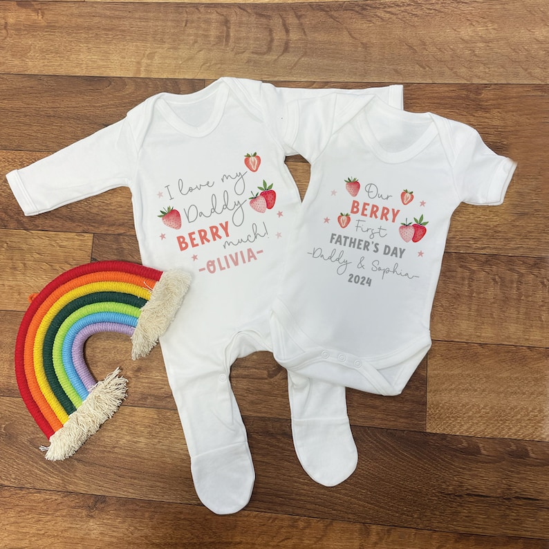 May include: Two white baby onesies with strawberry graphics and text. One onesie says "I love my Daddy Berry much! -Olivia-". The other onesie says "Our Berry First Father's Day -Daddy & Sophia- 2024".