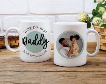 以下が含まれることがあります： 片側に父と娘の写真、反対側に「World's Best Daddy Love From Aliyah」という文字が書かれた白いセラミック製のマグカップです。