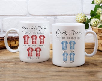 Op de afbeelding: Twee witte keramische mokken met een tie-dye ontwerp. De mokken hebben de tekst "Grandad's Team - Top of the League" en "Daddy's Team - Top of the League" met namen en nummers op elke mok.