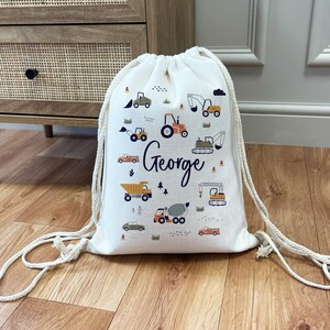 May include: A white drawstring bag with a design of construction vehicles and the name "George" printed on it.