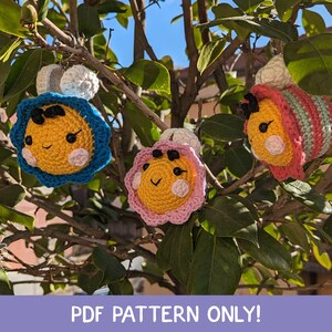 Può includere: Tre ornamenti a forma di ape all'uncinetto fatti a mano in giallo, blu e rosa, appesi a un ramo. Ogni ape ha una faccia sorridente ed è circondata da un bordo all'uncinetto. Il testo "PDF PATTERN ONLY!" è in basso.