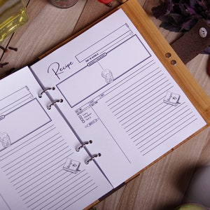 May include: Open recipe journal with lined pages and a wooden cover. The word "Recipe" is written in cursive. The journal is open to a page with a recipe diagram and a section for ingredients. A leather strap with a snap closure is visible.