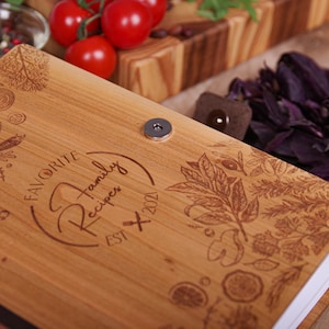 May include: A wooden recipe book with the words "Favorite Family Recipes EST 2021" engraved on the cover. The cover features engraved illustrations of herbs and spices. A magnetic clasp secures the book.