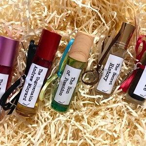 May include: Six small glass bottles with roll-on applicators, each containing a different scented oil. The bottles are labeled with the names of books: "The Ungovernable, Andrew Minyard", "The Son of Poseidon", "The Secret History", "Nevermore", and "The Birth of Venus".