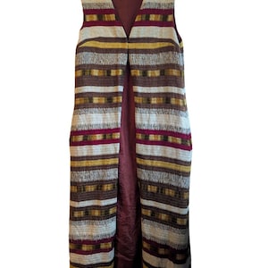 Peut inclure: Un long gilet sans manches avec un col en V, présentant un motif à rayures dans les tons marron, crème, jaune et bordeaux. Le gilet a une doublure bordeaux unie et est suspendu à un cintre en bois. Le vêtement semble être vintage.