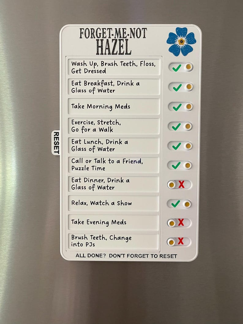 May include: A white magnetic daily checklist with the text "FORGET-ME-NOT HAZEL". The checklist includes tasks like "Wash Up, Brush Teeth, Floss, Get Dressed" and "Eat Breakfast, Drink a Glass of Water". A blue flower graphic is in the upper right corner.