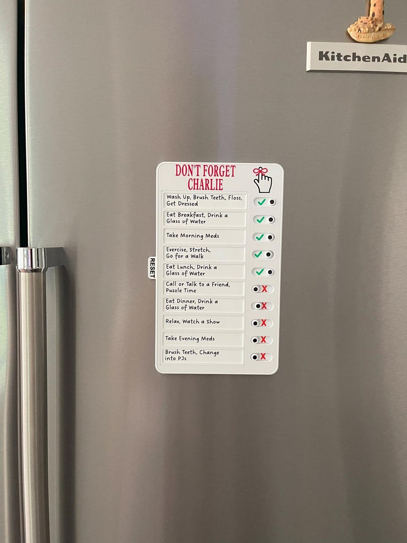 May include: A white magnetic checklist with the text "DON'T FORGET CHARLIE" and daily tasks. The checklist includes tasks like "Wash Up, Brush Teeth, Floss, Get Dressed" and "Take Morning Meds". Check marks and X's indicate completed tasks.