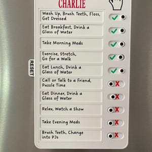 May include: A white magnetic chore chart with the text "DON'T FORGET CHARLIE" in red. The chart includes a list of daily tasks with check boxes. The tasks include "Wash Up, Brush Teeth, Floss, Get Dressed" and "Eat Breakfast, Drink a Glass of Water."