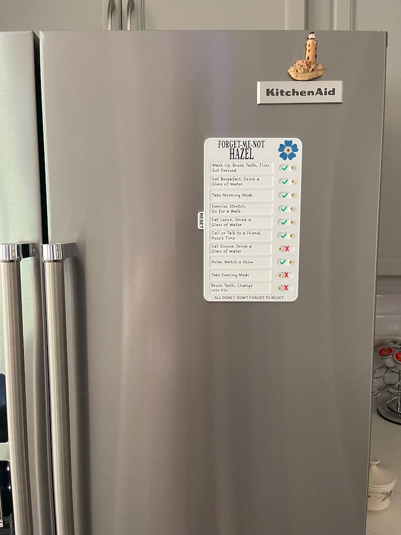 May include: A stainless steel refrigerator with a magnetic checklist that reads "FORGET-ME-NOT HAZEL". The checklist includes daily tasks with checkmarks and X's. A KitchenAid magnet and a lighthouse magnet are also on the refrigerator.