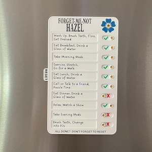 May include: A white magnetic checklist with the text "FORGET-ME-NOT HAZEL" and daily tasks. The checklist includes a blue flower graphic and check boxes with green check marks and red X's. The checklist is on a silver refrigerator.