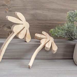 May include: Two wooden flower-shaped wall decor pieces in a natural wood finish. The pieces are arranged on a gray wooden surface with a small potted bonsai tree in the background.