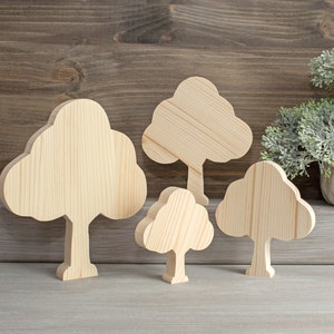 Könnte beinhalten: Vier ausgeschnittene Bäume aus Holz in verschiedenen Größen, in hellbrauner Farbe und mit glatter Oberfläche. Die Bäume sind auf einer hellgrauen Oberfläche angeordnet.