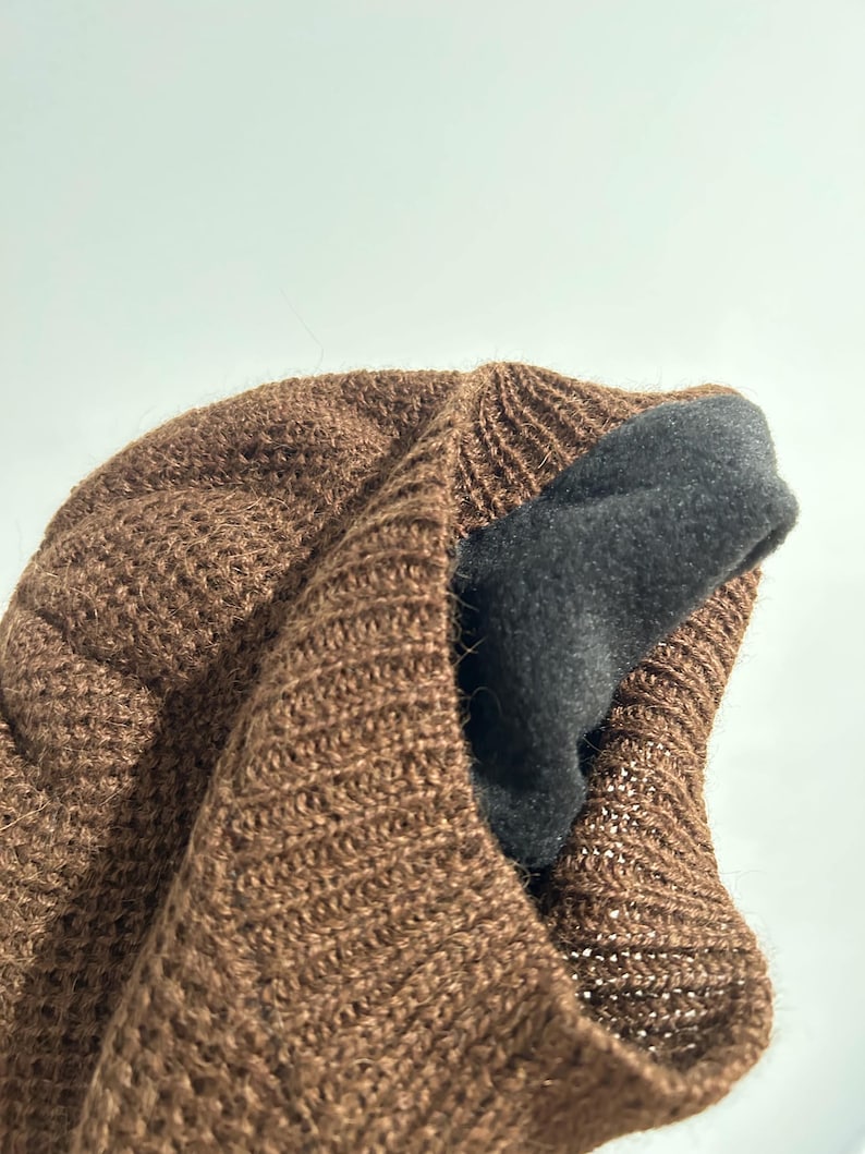 K&ouml;nnte beinhalten: Eine braune Strickm&uuml;tze mit einem dunkelgrauen Fleecefutter. Die M&uuml;tze besteht aus einem strukturierten Material mit offener Webart. Das Innenfutter ist sichtbar und bietet W&auml;rme und Komfort.