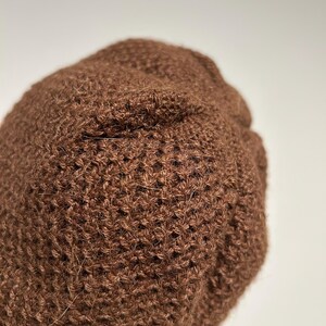 K&ouml;nnte beinhalten: Nahaufnahme einer braunen Strickm&uuml;tze. Die M&uuml;tze besteht aus einem strukturierten, gewebten Material. Die M&uuml;tze hat eine einfarbige braune Farbe und scheint handgefertigt zu sein. Die M&uuml;tze ist ein Winteraccessoire.