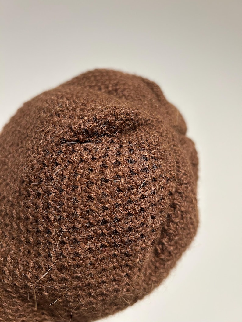 K&ouml;nnte beinhalten: Nahaufnahme einer braunen Strickm&uuml;tze. Die M&uuml;tze besteht aus einem strukturierten, gewebten Material. Die M&uuml;tze hat eine einfarbige braune Farbe und scheint handgefertigt zu sein. Die M&uuml;tze ist ein Winteraccessoire.