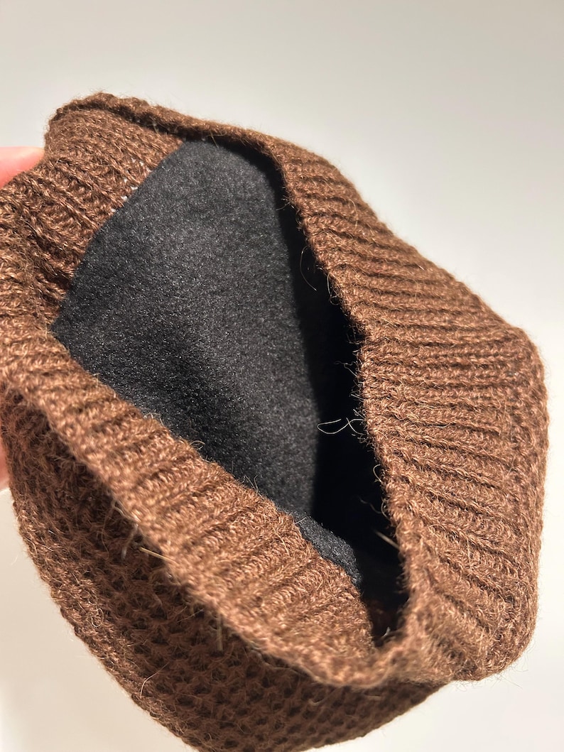 K&ouml;nnte beinhalten: Eine braune Strickm&uuml;tze mit schwarzem Innenfutter. Die M&uuml;tze besteht aus einem strukturierten, gerippten Strickmaterial. Das Innenfutter ist dunkel und einfarbig. Die M&uuml;tze scheint umgeschlagen zu sein.