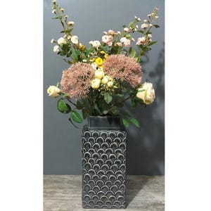May include: A black ceramic vase with a textured, scale-like pattern. The vase is filled with a bouquet of pink, white and yellow flowers.