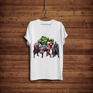 May include: White t-shirt featuring a graphic of several superheroes, including the Hulk, Thor, Captain America, Iron Man, and Batman. The shirt is hanging on a hanger against a wooden background. The superheroes are in their iconic costumes.