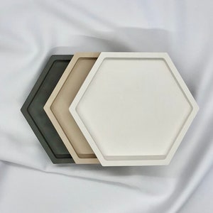 Puede incluir: Tres bandejas hexagonales apiladas una encima de la otra. La bandeja superior es blanca, la bandeja del medio es beige y la bandeja inferior es gris oscuro.