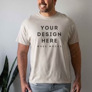 Könnte beinhalten: Ein beiges T-Shirt mit dem Text "YOUR DESIGN HERE" und "MUSE MOCKS" auf der Vorderseite.