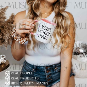 May include: A white ceramic mug with a pink rim and handle. The mug has the text "YOUR DESIGN HERE" in colorful letters. The mug is being held by a person wearing a white tank top and denim shorts.