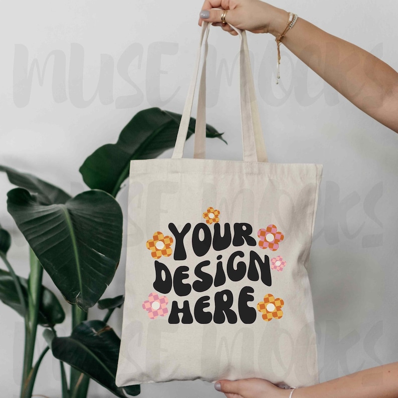 May include: A white canvas tote bag with black text that says "Your design here" and colorful flower graphics.