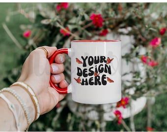 May include: White ceramic mug with a red rim and handle. The mug has a black graphic that says "YOUR DESIGN HERE" with orange butterflies around the text.