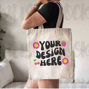 May include: A white canvas tote bag with black text that says "Your Design Here" and pink and yellow flower and cherry graphics.