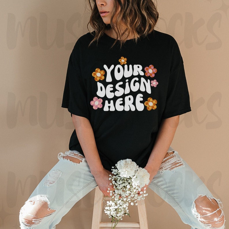 K&ouml;nnte beinhalten: Ein schwarzes T-Shirt mit einem grafischen Design, das "Your Design Here" in einer Retro-Schriftart mit bunten Blumen um den Text herum sagt.