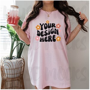 May include: A pink oversized t-shirt with the text "YOUR DESIGN HERE" in black with colorful flower graphics.