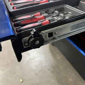 May include: A partially open blue toolbox drawer filled with various tools. The tools have black handles with red accents. The drawer is lined with gray foam to hold the tools in place. The drawer's metal slide is visible.