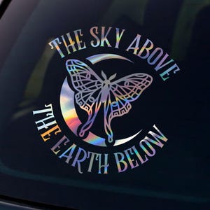 May include: A holographic vinyl decal featuring a moth design within a crescent moon, with the text "THE SKY ABOVE THE EARTH BELOW." The decal is affixed to the rear window of a black vehicle, set against a scenic sunset.