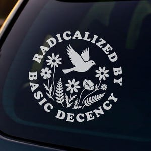 May include: A white circular vinyl decal applied to a car rear window. The design features a central illustration of a bird surrounded by various flowers and leaves, with the text RADICALIZED BY BASIC DECENCY arranged in a circular border.
