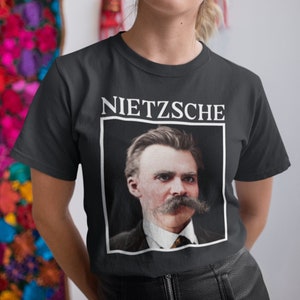 May include: A black t-shirt featuring a white graphic of a portrait of Friedrich Nietzsche with the word "NIETZSCHE" printed above the portrait.