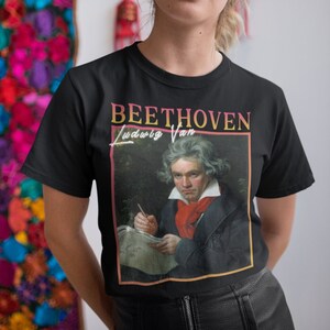 May include: A black t-shirt featuring a vintage-style graphic of Ludwig van Beethoven. The graphic includes a portrait of Beethoven and the text "BEETHOVEN Ludwig Van".