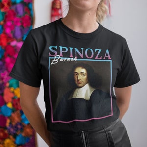 Può includere: Maglietta nera con una stampa grafica di Baruch Spinoza, un filosofo, con il testo "Spinoza Baruch" in lettere rosa e blu.