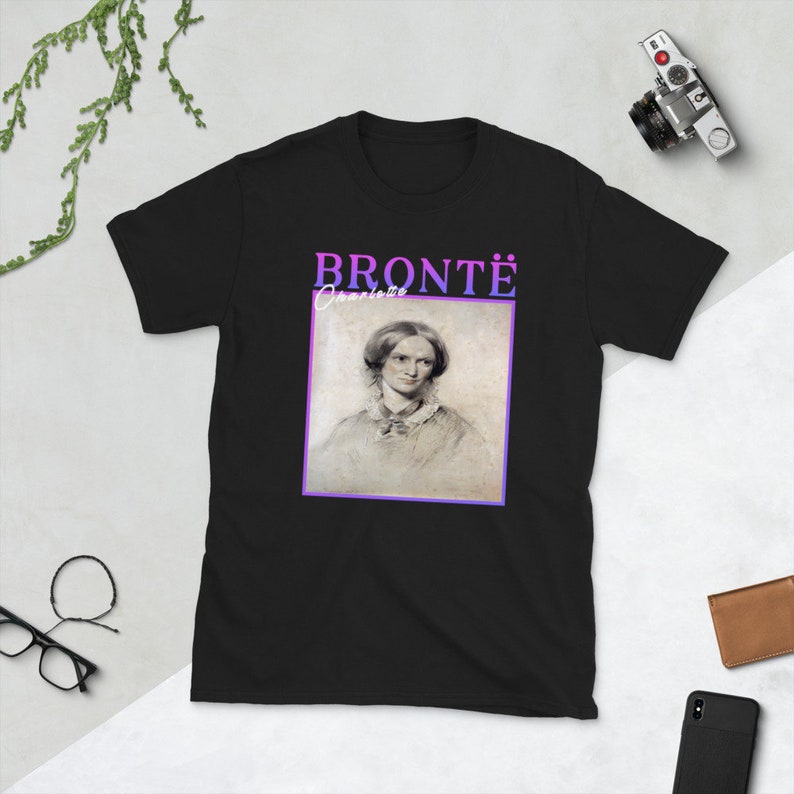 Pode incluir: Camiseta preta com um retrato de Charlotte Bront&euml; em uma moldura branca. O texto "BRONT&Euml;" est&aacute; acima do retrato em letras roxas e rosas. O texto "Charlotte" est&aacute; abaixo do retrato em letras brancas.