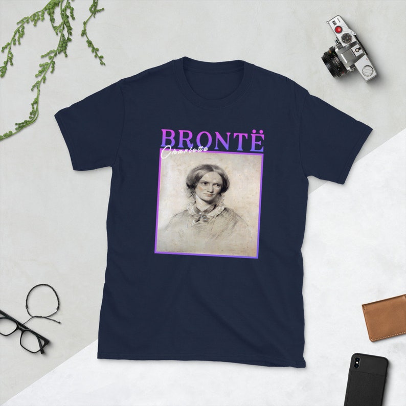 Pode incluir: Uma camiseta azul marinho com um retrato de Charlotte Bront&euml; e o texto "BRONT&Euml; Charlotte" em um degrad&ecirc; roxo e rosa.