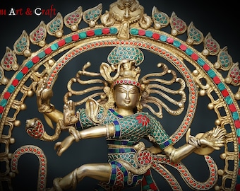 May include: A gold-toned metal sculpture of a Hindu deity, Shiva Nataraja, in a dancing pose. The sculpture is adorned with colorful gemstones and intricate details. The sculpture is set against a dark background.
