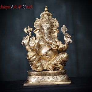May include: A gold-colored brass statue of Ganesha, the Hindu god of wisdom and prosperity, sitting on a pedestal. The statue is intricately detailed with ornate carvings and decorations.