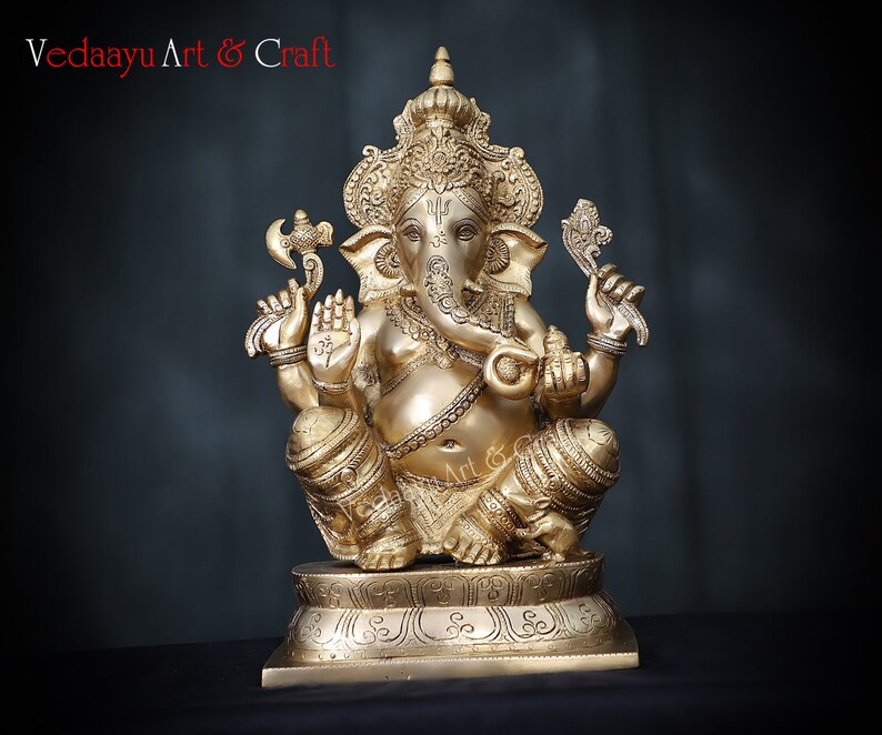 May include: A gold-colored brass statue of Ganesha, the Hindu god of wisdom and prosperity, sitting on a pedestal. The statue is intricately detailed with ornate carvings and decorations.