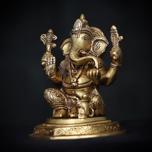 Op de afbeelding: Een gouden beeld van Ganesha, de hindoe&iuml;stische god van wijsheid en voorspoed, zittend op een basis met ingewikkelde details. Het beeld is gemaakt van metaal en heeft een gedetailleerd ontwerp.