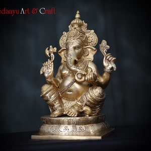 May include: A gold-colored brass statue of Ganesha, the Hindu god of wisdom and prosperity, sitting on a pedestal with intricate carvings. The statue is detailed with ornate jewelry and a trunk.
