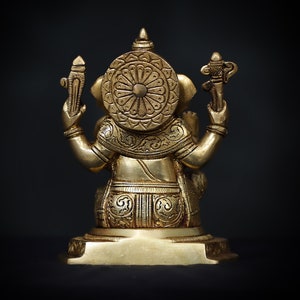 Op de afbeelding: Een gouden metalen beeld van Ganesha, de hindoe&iuml;stische god van wijsheid en voorspoed, zittend op een voetstuk. Het beeld is ingewikkeld versierd met bloem- en geometrische patronen.