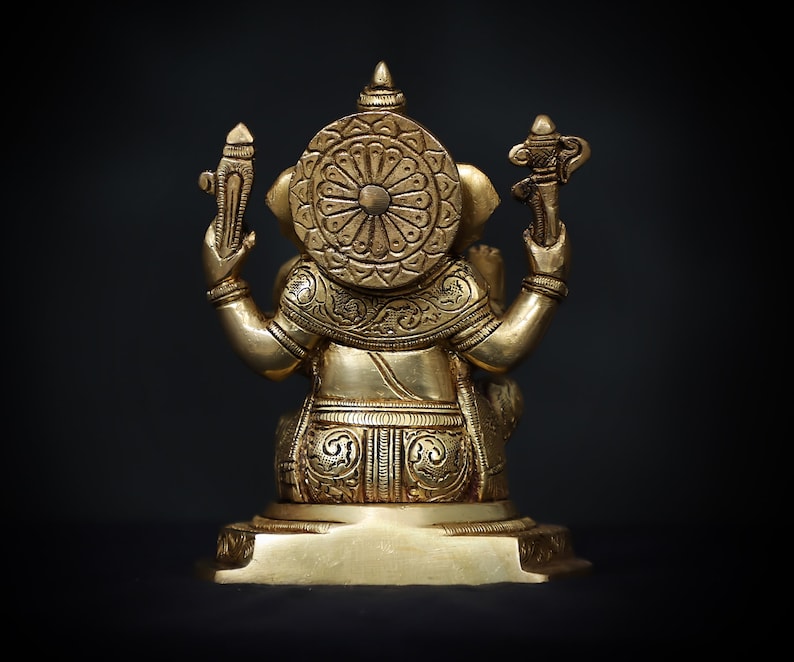 Op de afbeelding: Een gouden metalen beeld van Ganesha, de hindoe&iuml;stische god van wijsheid en voorspoed, zittend op een voetstuk. Het beeld is ingewikkeld versierd met bloem- en geometrische patronen.
